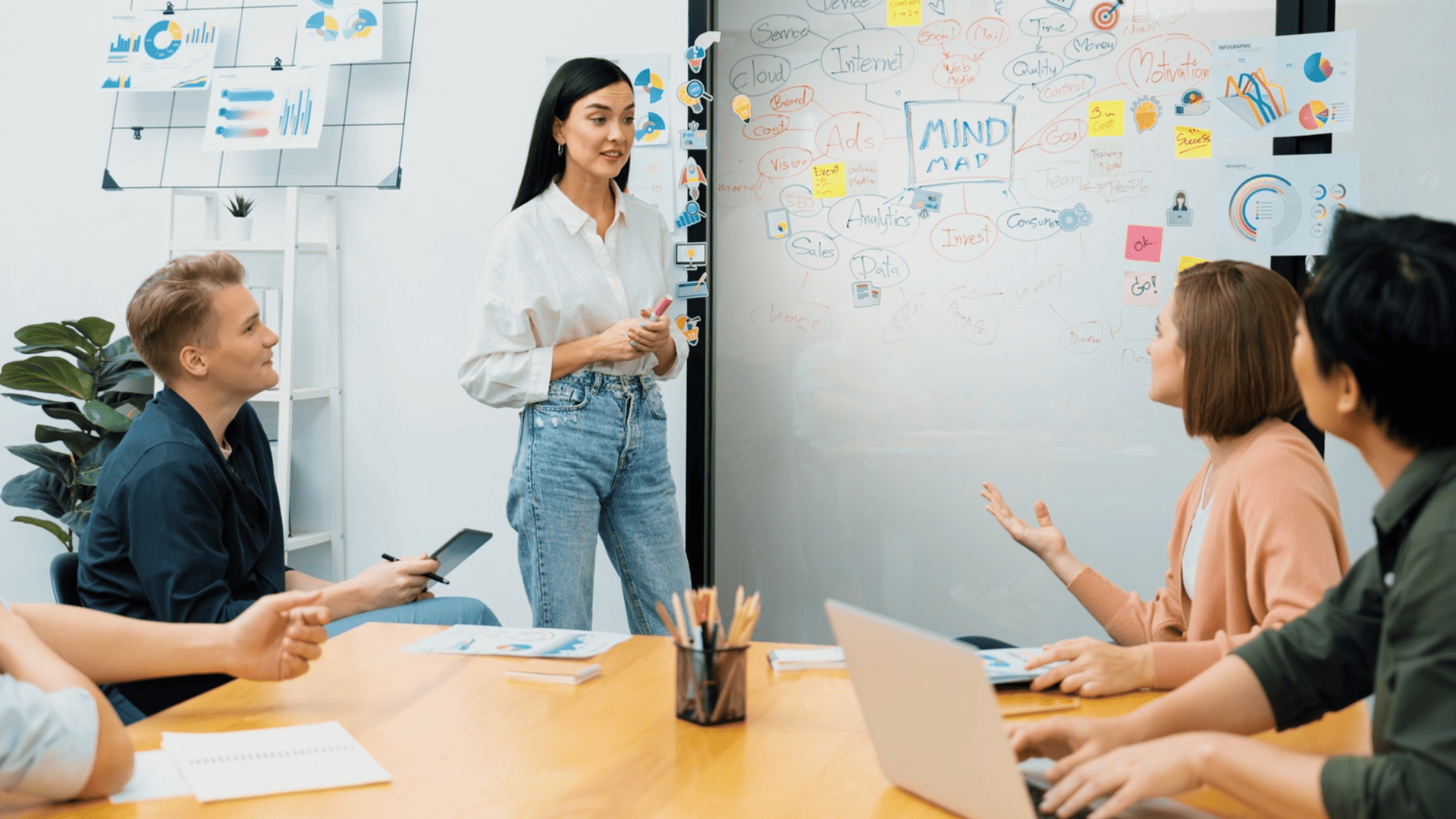 a group of people having a meeting, and a girl standing in front, while others listen to her