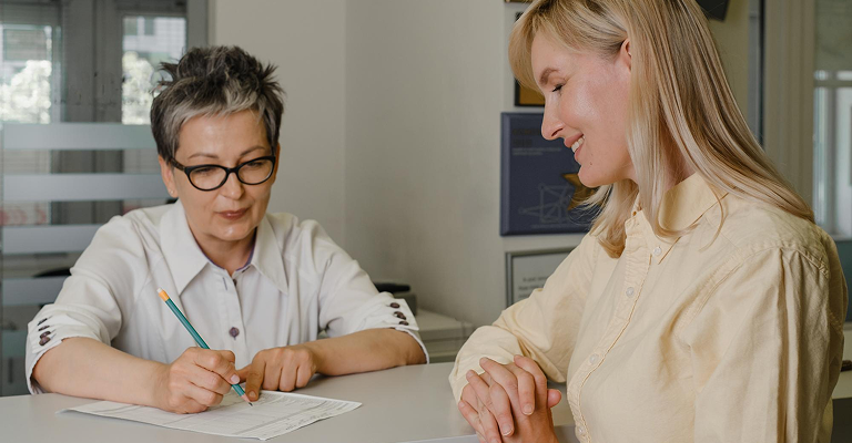 a woman writing on the paper while the other woman looking at her